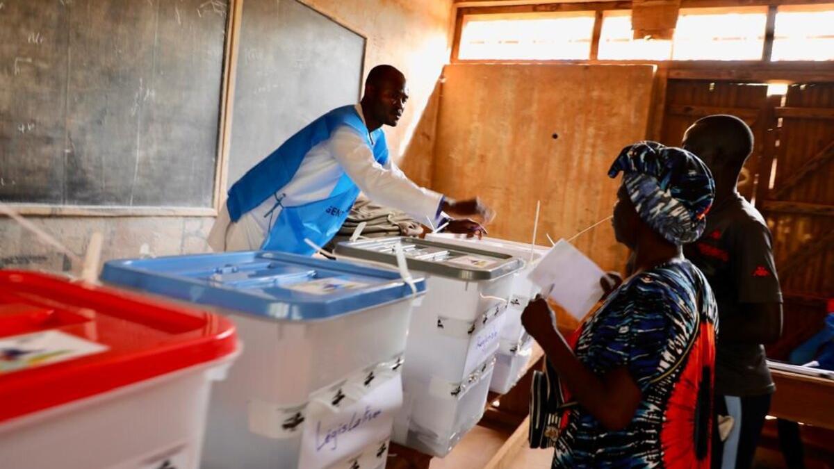 Un agent électoral aide des électeurs à déposer leurs bulletins.
