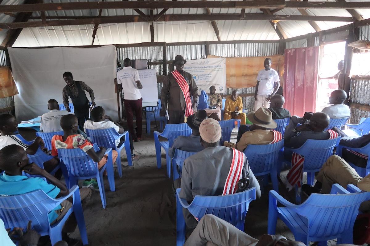 With tensions rising in South Sudan, people in Leer County call on local and national leaders to reach agreements through dialogue for peace to prevail. Photos: Jacob Ruai/UNMISS A group of people seated in blue chairs facing the front of the room where a presentation is being given.